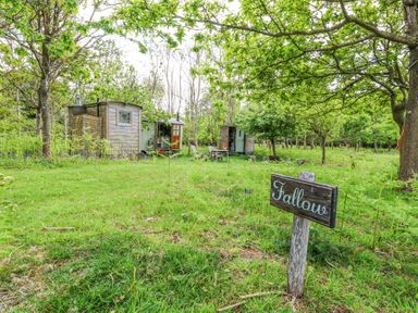 A grassy outdoor area with trees wooden huts and a sign reading Fallow at Warmwell