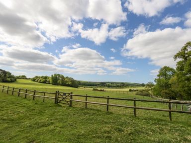 A grassy field with a wooden fence and gate under a partly cloudy sky at Fallow in Warmwell