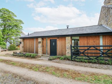 The exterior of a single-story wooden building with a black door and a black gate beside it at The Barn Riding Mill near Corbridge