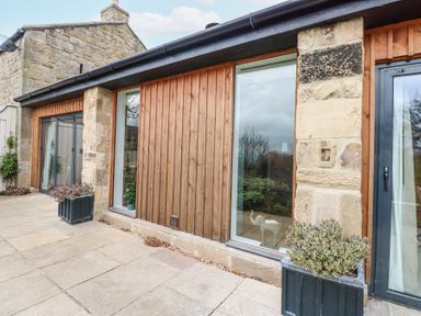 A stone and wood exterior wall with large windows and black planters with plants at The Barn in Riding Mill near Corbridge
