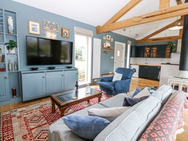A living room with a sofa, blue armchair, coffee table, large TV on a blue cabinet, and open kitchen at The Barn in Riding Mill near Corbridge