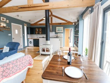 A dining table set with plates and wine in a room with a kitchen stove and exposed wooden beams at The Barn Riding Mill near Corbridge