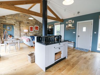An open living space with a kitchen island a dining table a sofa and wooden beams at The Barn Riding Mill near Corbridge