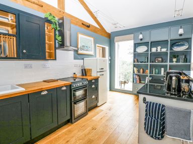 A kitchen with dark cabinets wooden countertops a white refrigerator open shelves and a window at The Barn Riding Mill near Corbridge