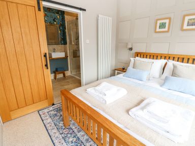 A bedroom with a wooden bed and folded towels on the bed next to a sliding wooden door leading to a bathroom at The Barn in Riding Mill near Corbridge
