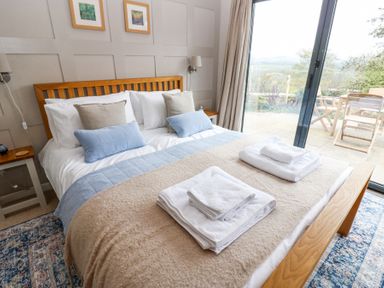 A bedroom with a wooden bed frame white and blue bedding folded towels on the bed and a glass door leading outside at The Barn in Riding Mill near Corbridge