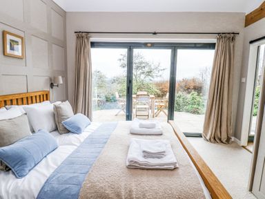 A bedroom with a bed arranged with pillows and towels and a patio with a table and chairs seen through sliding glass doors at The Barn Riding Mill near Corbridge