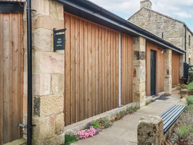 A stone and wood exterior of a building with a black door and a sign that reads The Barn Riding Mill near Corbridge