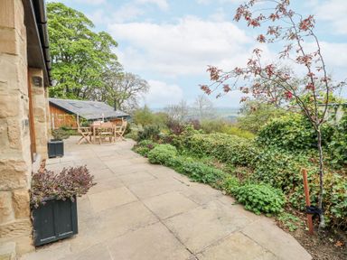 A stone patio with wooden outdoor furniture and plants surrounding the area at The Barn in Riding Mill near Corbridge