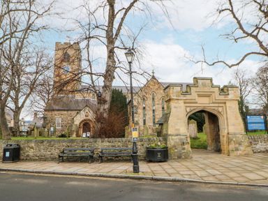A stone church with a clock tower and arched entrance behind a stone wall with benches and a lamppost at The Barn in Riding Mill near Corbridge