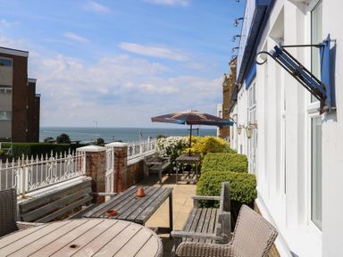 An outdoor patio with tables benches chairs umbrella and plants overlooking the sea at The Burleigh in Hunstanton