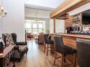 A bar area with stools and bottles behind the counter next to a seating area with chairs and tables at The Burleigh in Hunstanton