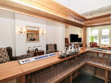 A home bar setup with taps glasses and seating area with armchairs and TV at The Burleigh in Hunstanton