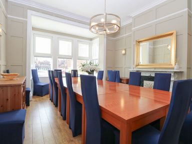 A dining room with a long wooden table and blue covered chairs and a large mirror above a fireplace at The Burleigh in Hunstanton
