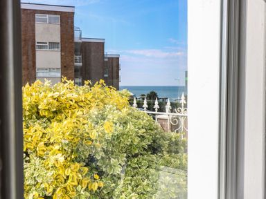 View through a window showing yellow and green bushes a railing a brick building and the sea in the background at The Burleigh in Hunstanton