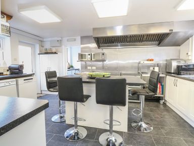 A kitchen with a central island and four black bar stools microwaves and various appliances at The Burleigh in Hunstanton