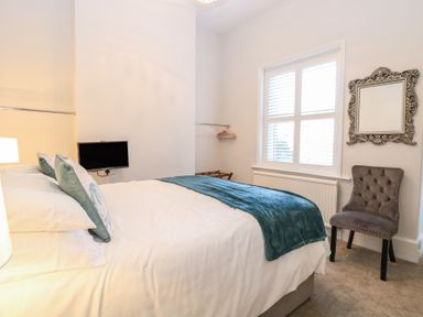 A bedroom with a bed cushions a blanket a small television a chair a mirror and a window at The Burleigh in Hunstanton