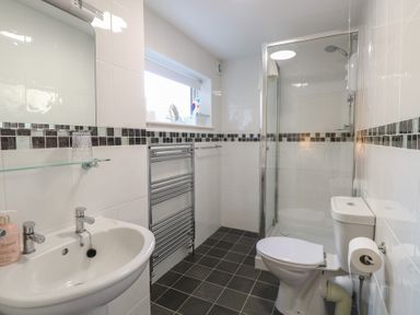 A bathroom with a sink toilet shower glass shelf towel rack and window at The Burleigh in Hunstanton