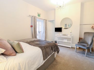 A bedroom with a bed pillows a chair a dresser with a mirror and a television at The Burleigh in Hunstanton