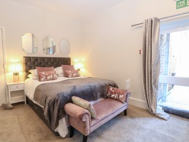A bedroom with a bed two bedside tables lamps three mirrors and a bench at The Burleigh in Hunstanton