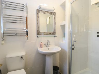 A bathroom with a toilet, pedestal sink, wall mirror, glass shower enclosure, and a heated towel rack at The Burleigh in Hunstanton
