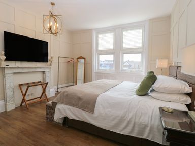 A bedroom with a bed and green pillow near windows a television above a fireplace and a standing mirror at The Burleigh in Hunstanton