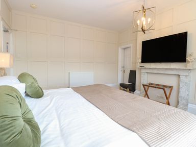 A bedroom with a bed green pillows a wall-mounted television and a fireplace at The Burleigh in Hunstanton