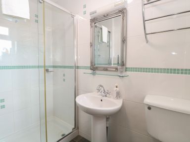 A bathroom with a shower enclosure, pedestal sink, toilet, and decorative mirror at The Burleigh in Hunstanton