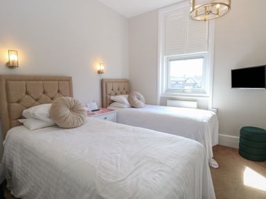 A bedroom with two single beds cushions wall lights window and a wall mounted tv at The Burleigh in Hunstanton
