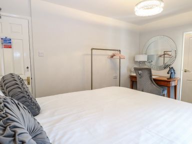 A bedroom with a bed white bedding and grey pillows a wooden desk with a grey chair and a round mirror on the wall at The Burleigh in Hunstanton
