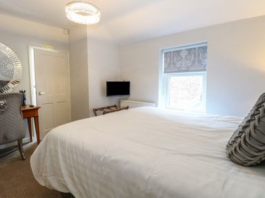 A bedroom with a bed a window a wall mounted tv a chair a wooden desk and a decorative round mirror at The Burleigh in Hunstanton