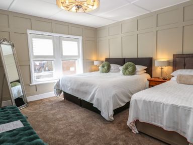 A bedroom with two beds a large mirror bedside tables with lamps and a window with blinds at The Burleigh in Hunstanton