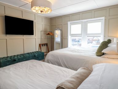 A bedroom with two beds a wall mounted television a full length mirror and a window at The Burleigh in Hunstanton