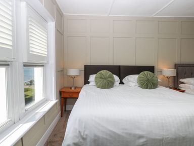 A bedroom with a large bed two green round cushions two bedside tables with lamps and windows with shutters at The Burleigh in Hunstanton