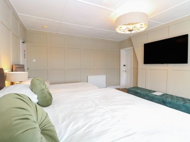 A bedroom with two beds green round pillows a wall-mounted television and a long green bench at The Burleigh in Hunstanton