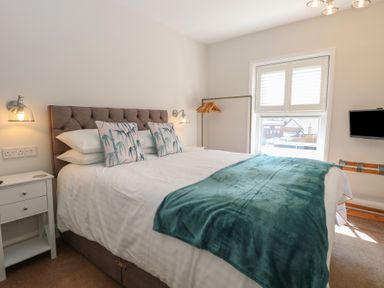 A bedroom with a bed with white sheets and a green throw blanket a nightstand with lamps and a window with shutters at The Burleigh in Hunstanton