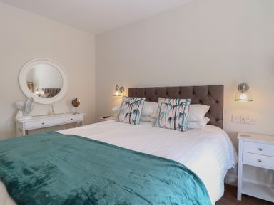 A bedroom with a bed with teal blanket and patterned pillows two bedside tables and a round mirror at The Burleigh in Hunstanton