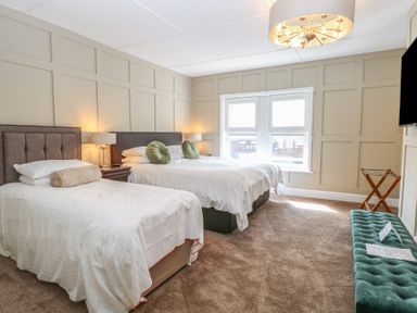A bedroom with two beds lamps a window and a bench at The Burleigh in Hunstanton