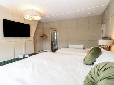 A bedroom with two beds a wall-mounted television a lamp and a clothes rack at The Burleigh in Hunstanton