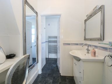 A bathroom with a sink and mirror and an adjacent room with a towel rack and tiled walls at The Burleigh in Hunstanton