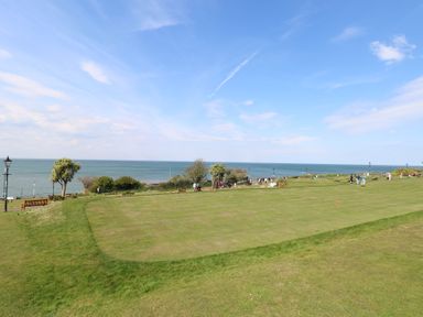A grassy park area with people walking and benches near the sea at The Burleigh in Hunstanton
