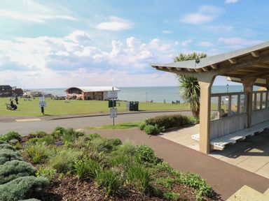 A seaside park with a shelter on the right and a building in the distance at The Burleigh in Hunstanton