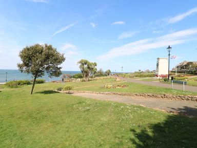 A park with grass, trees, benches, a monument, and a path by the sea at The Burleigh in Hunstanton