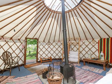 The interior of a yurt with a wood stove in the center rugs on the floor a wooden chair and a table with lanterns at Moonlight in Ventnor