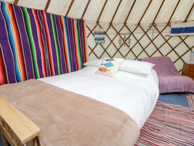 A bed with white linens and a fish pillow inside a yurt with a colorful striped blanket on the wall and a purple covered chair at Moonlight in Ventnor
