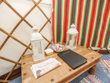 A wooden table with two white lanterns a bowl of shells a folded newspaper and a black book inside a yurt at Moonlight in Ventnor