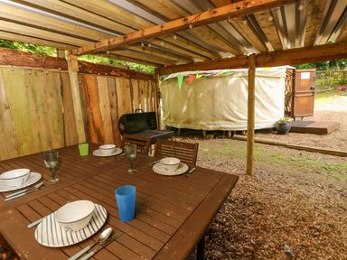 An outdoor covered dining area with a wooden table set with plates bowls cups and cutlery a barbecue grill and a round tent outside at Moonlight in Ventnor