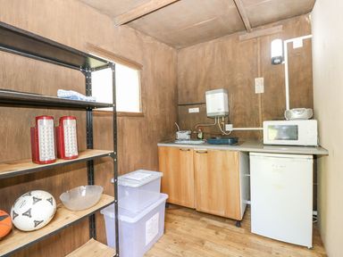 A small kitchen area with wooden cabinets a mini fridge microwave sink shelving unit with soccer balls and plastic storage containers at Moonlight in Ventnor