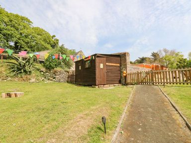 A garden area with a wooden shed labeled washrooms a paved pathway and colorful bunting at Moonlight in Ventnor