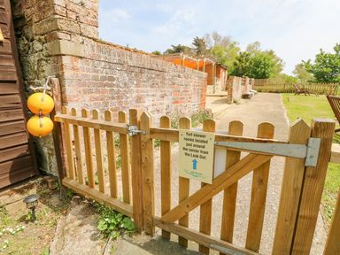 A wooden gate with a sign about yurt shower rooms attached to a brick wall and a garden area at Bank End Farm